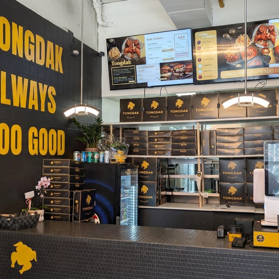 Tongdak restaurant counter with black-and-yellow branding, digital menus, packaged food boxes, and a self-ordering kiosk.